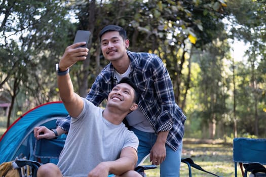 Asian LGBTQ couple tent in front of camp talking on smartphone in video chat or take a selfie.
