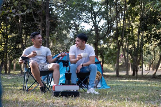 Asian LGBTQ couple drinking coffee in a romantic camping tent. LGBTQ couple drinking coffee in a camping tent, enjoying nature, forest, camping atmosphere, LGBTQ, gay, gay men..