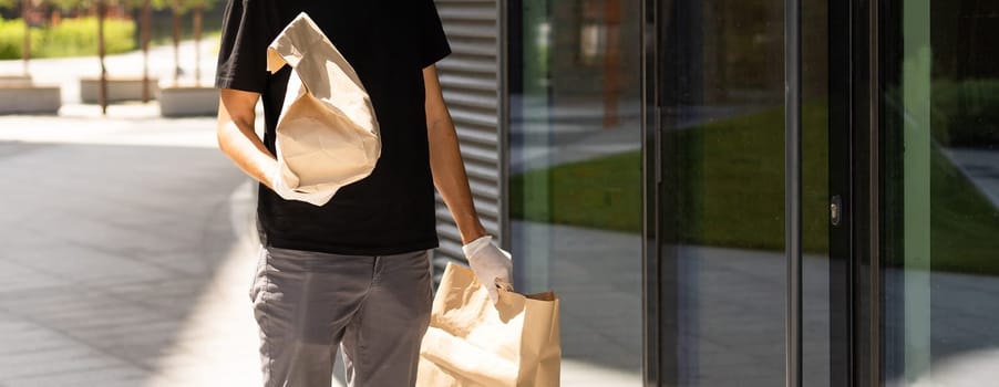 Contactless delivery during COVID-19 pandemic lockdown concept. Courier wearing mask and gloves holds a parcel box and checking address details on the smartphone.