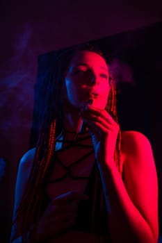 Profile of caucasian girl with dreadlocks smokes a vape in red blue light