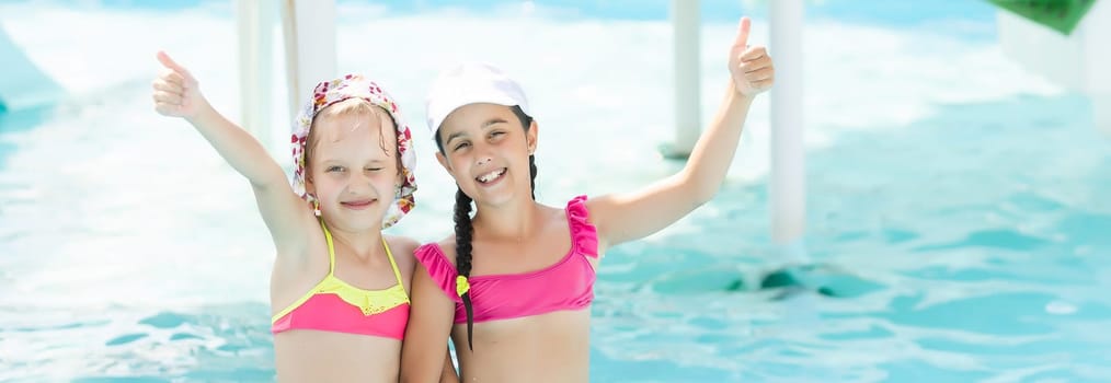 two girls splash in an outdoors swimming pool in summer. Happy children, sister playing, enjoying sunny weather in public pool.
