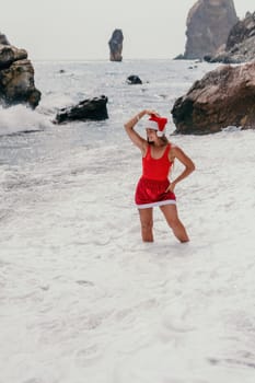 Woman travel sea. Young Happy woman in a long red dress posing on a beach near the sea on background of volcanic rocks, like in Iceland, sharing travel adventure journey