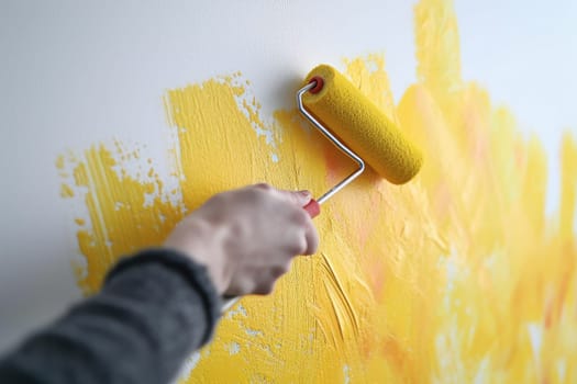 A moment of creativity when a hand with a paint roller paints the wall bright yellow.