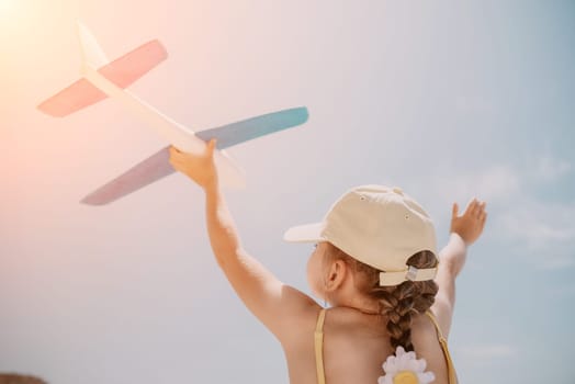 Kid playing with toy airplane. Children dream of travel by plane. Happy child girl has fun in summer vacation by sea and mountains. Outdoors activities at background of blue sky. Lifestyle moment