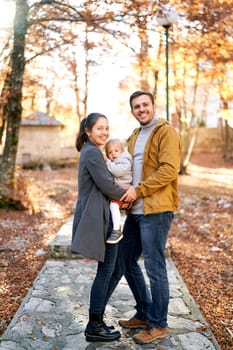 Smiling dad holding mom hand with a little girl in her arms while standing in an autumn park. High quality photo