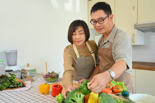 Attractive senior couple in casual outfits cooking together in kitchen. Healthy lifestyle concept.