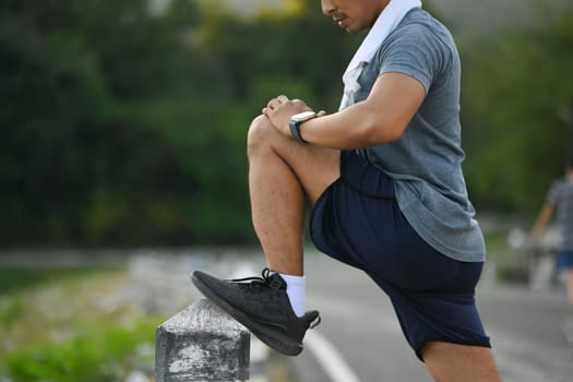 Young sportsman stretching legs in the park before running at morning.