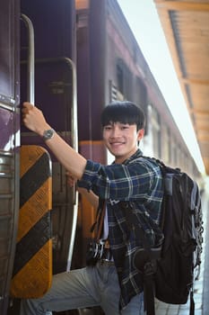 Portrait of happy male traveler with a backpack getting on the train. Travel and vacations concept
