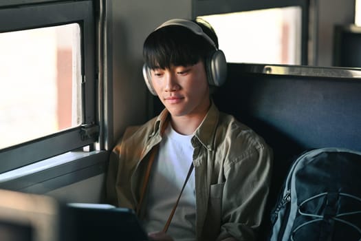 Young man in headphone using digital tablet while commuting by train. Travel and transportation concept.