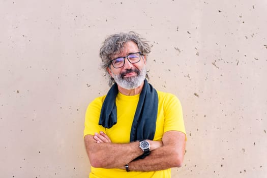 senior sports man with glasses leaning on a wall with arms crossed looking at camera, concept of active and healthy lifestyle on the middle age, copy space for text