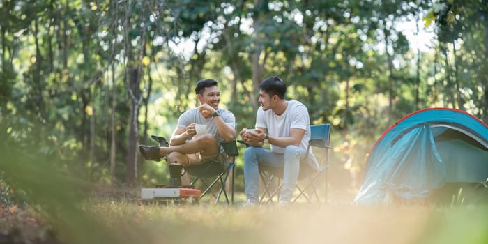 Gay LGBTQIA couple sitting on picnic chair drinking tea and coffee while camping on vacation holiday.