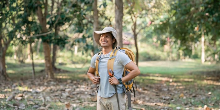 Young man backpacker traveling alone in forest. Attractive male traveler walking in nature wood during holiday vacation trip.