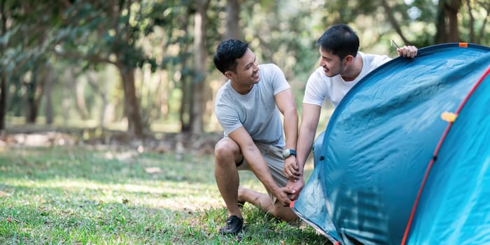 LGBTQIA Gay couple camping together in woods for holidays and helping set up a tent together.