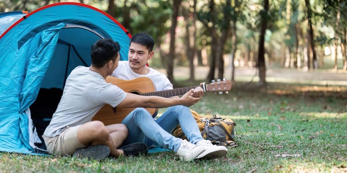 LGBTQIA Gay couple camping together in woods for holidays and relax on guitar together.