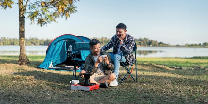 Gay LGBTQIA couple sitting on picnic chair drinking tea and coffee while camping on vacation holiday.
