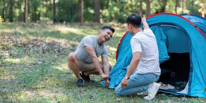 LGBTQIA Gay couple camping together in woods for holidays and helping set up a tent together.