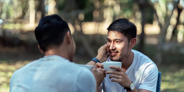 Gay LGBTQIA couple sitting on picnic chair drinking tea and coffee while camping on vacation holiday.