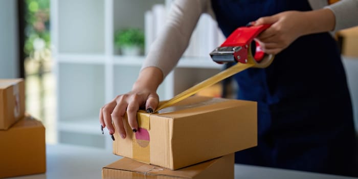 Woman use scotch tape to attach parcel box to prepare goods for the process of packaging, shipping, online sale internet marketing ecommerce concept startup business idea.