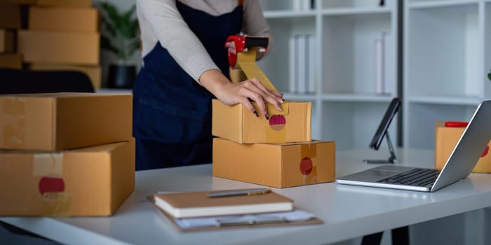 Woman use scotch tape to attach parcel box to prepare goods for the process of packaging, shipping, online sale internet marketing ecommerce concept startup business idea.