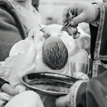 A priest pours water on the head of a small child during the Christian rite of baptism in the church, the baptism of an infant.