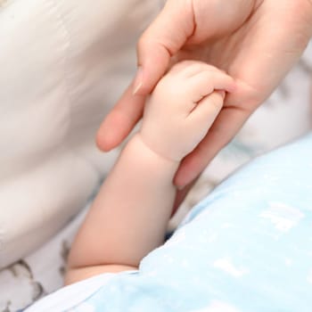 Small hand of a newborn baby close-up, mother supports the baby.