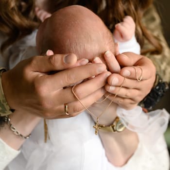 The parents hold the tiny head of their child in their hands, a gold cross and chain, jewelry hangs on their hands.