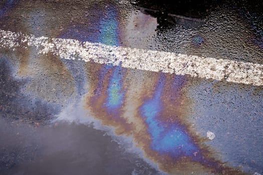 Oil spill on wet asphalt, parking lot with dividing line.