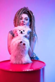 cool girl with braided dreadlocks on her head with a cute Pomeranian dog in neon light on a light background