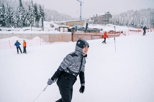 Smiling young woman pulling a sled with a rope up the mountain. Side view. High quality photo