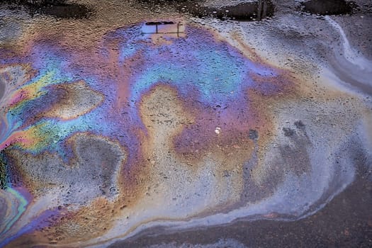 Background texture of an oil spill in the form of a rainbow stain on dark asphalt, parking.
