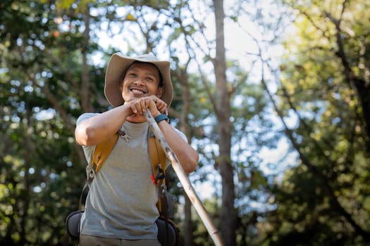 Young man asian trekking among trees with backpack, young man enjoy alone in forest. Camping, hiking, travelling, search for adventure concept.