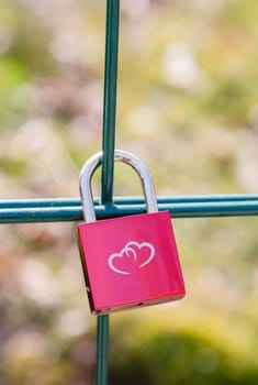 Pink metal lock on a fence in a park with an image of two hearts. Traditionally, people hang a padlock after a wedding to keep love in their hearts forever, Valentine's Day, High Quality Photo