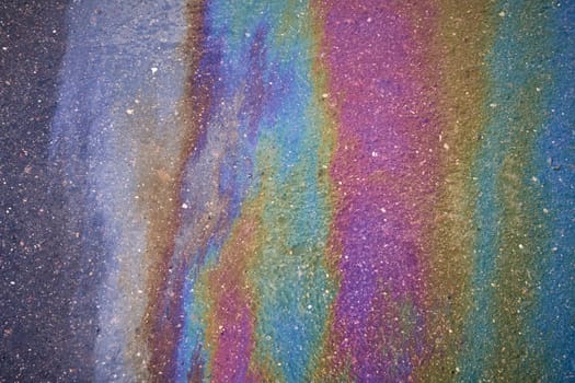 Gasoline spot on wet asphalt. Multi colored oil spill on asphalt road, abstract background, texture