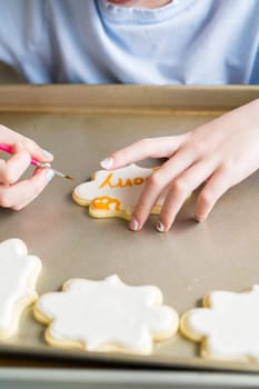 A heartwarming scene of a little girl carefully writing 'Sorry' on sugar cookies with food coloring, the cookies beautifully flooded with white royal icing.