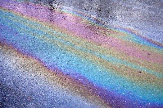 Background texture of an oil spill in the form of a rainbow stain on dark asphalt, parking. Selective focus