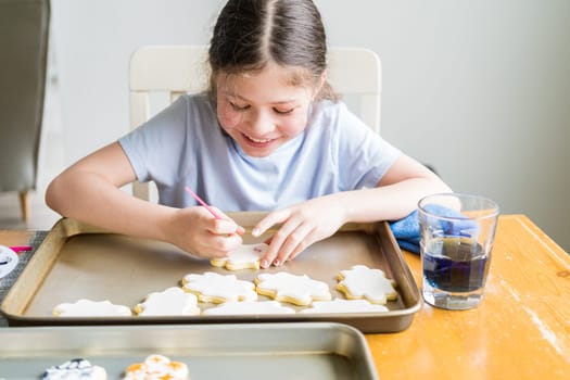 A heartwarming scene of a little girl carefully writing 'Sorry' on sugar cookies with food coloring, the cookies beautifully flooded with white royal icing.