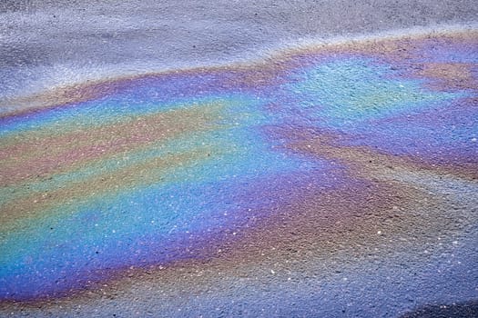 Background texture of an oil spill in the form of a rainbow stain on dark asphalt, parking..