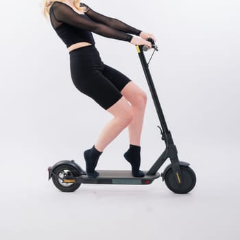 Female in a sport clothes stands on electric scooter with sunglasses on red and white background