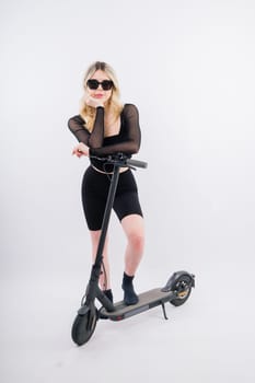Female in a sport clothes stands on electric scooter with sunglasses on red and white background