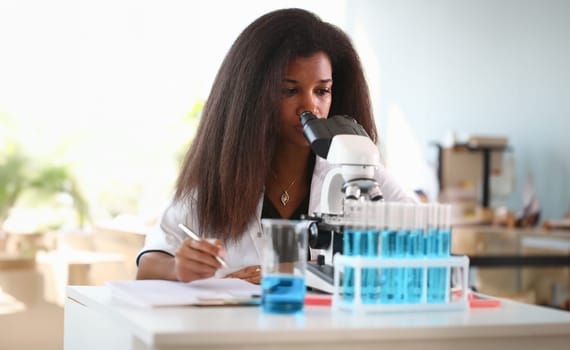 Black woman scientist student chemist in protective goggles are conducting research using microscope for bacterial contamination of water to search for vaccine to treat diseases in medicine.