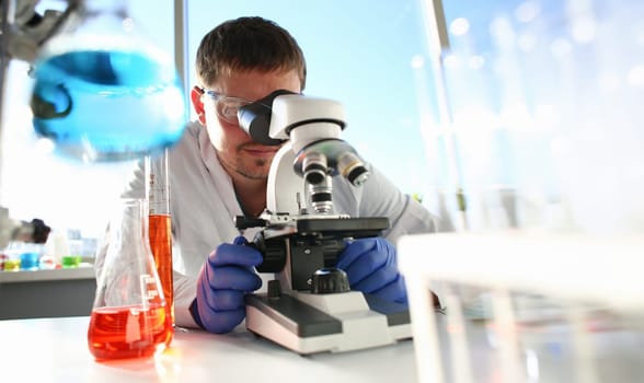 Portrait of a young chemist looking in binocular microscope looking for pathology analyzes patient at medical hospital for treatment disease tumors