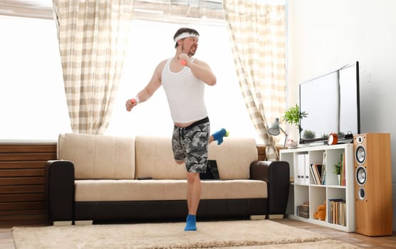 Young handsome man in shorts and vest holds pink dumbbells in hand. Watch tv lessons single combats is practicing receptions of sensei one home fitness indoor training independent education remotely