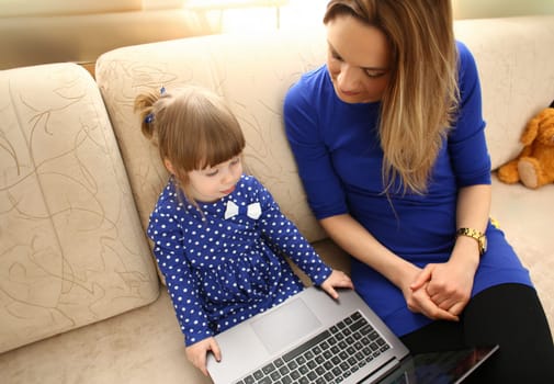 Cute little girl on couch with mom use laptop pc for chat with her dad away on business portrait. Point finger hand in display social web network bank mortgage credit wireless ip telephony concept