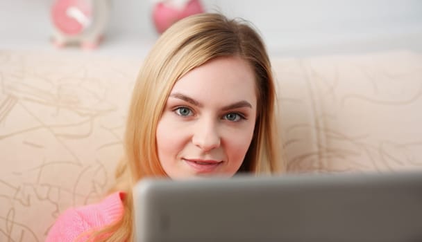 young beautiful blond woman sit on the sofa in livingroom hold tablet in arms sunny morning concept