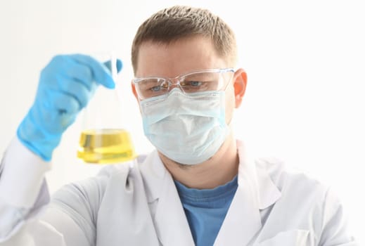 A portrait of a young surgeon chemist doctor looks at a container with a yellow liquid and a mask is fought with viruses and a vaccine for vaccines against diseases.