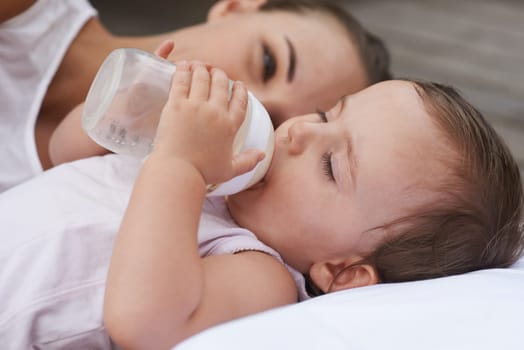 Calm, happy and a mother with a baby and milk for nutrition, health and growth development. Morning, family and a young mom and child with a bottle in the bedroom of a house for food and a drink.