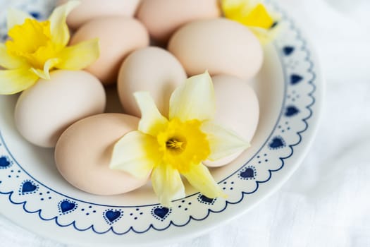 Fresh eggs and daffodils on a decorative plate, symbolizing spring or Easter. The plate is white with a blue pattern around the edge in the form of hearts and dots