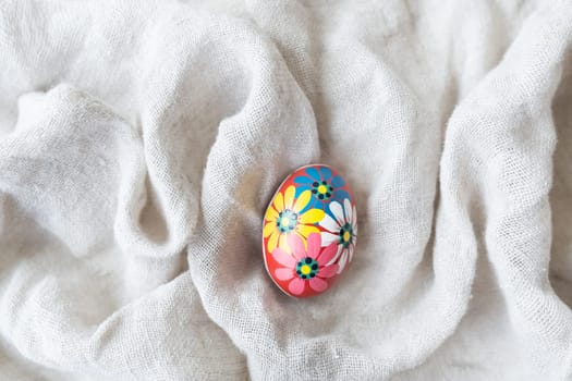 A colorful hand painted Easter egg with intricate floral designs on white fabric. The egg is decorated with flowers of different colors