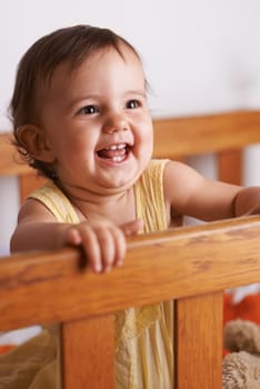 Excited baby in crib, playing with smile and fun in home, child development and care in home. Toddler girl in cot with playful face, energy and happiness in cute kids bedroom, nursery or apartment