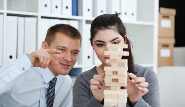 Businessman and businesswoman plays in strategy hand rearranging wooden blocks involved during break at work in office sitting table gaming pile fun joy pastime concept.